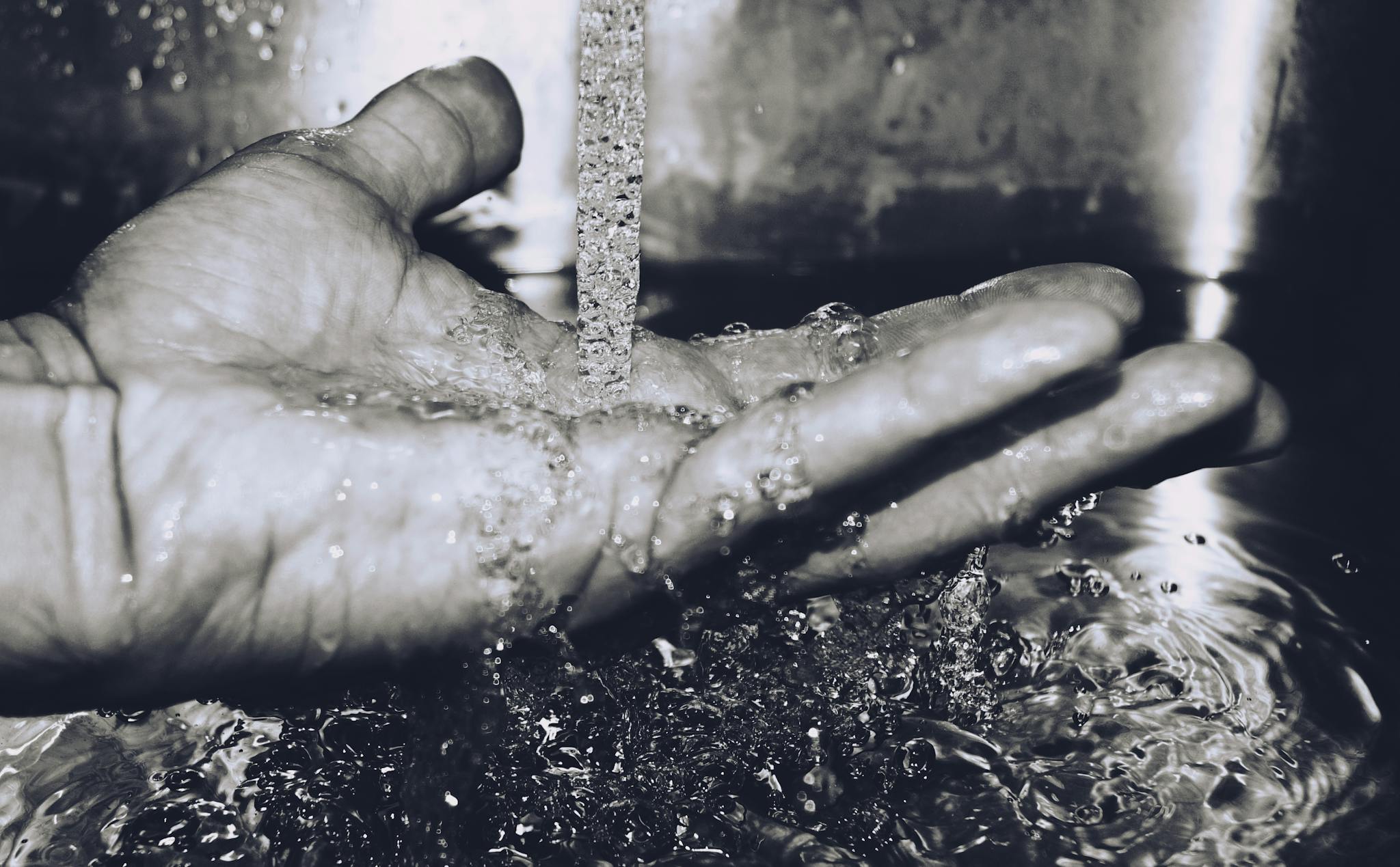 Black and white image of water flowing into a hand offering a sense of purity.